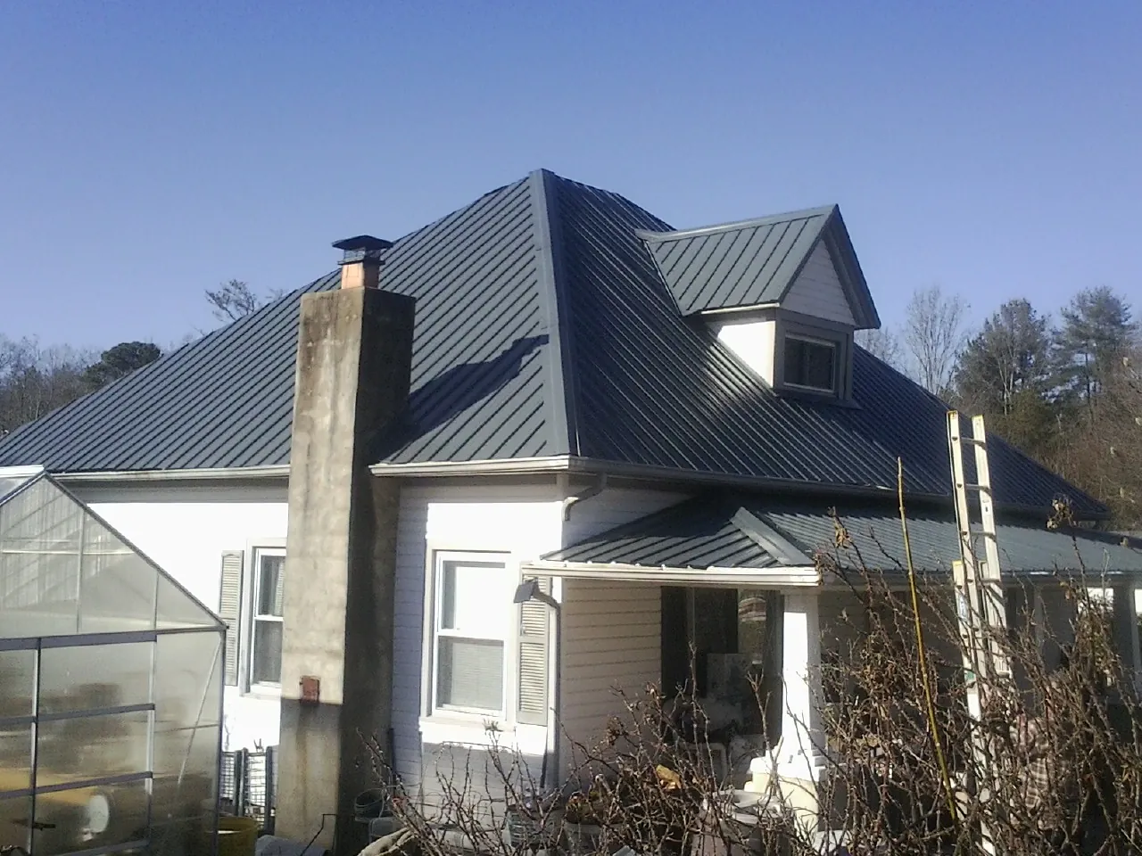 Dark blue standing seam metal roof on a white farmhouse with dormer — Slate & Tile Roof Repair by Roofing Brothers in Morse Bluff