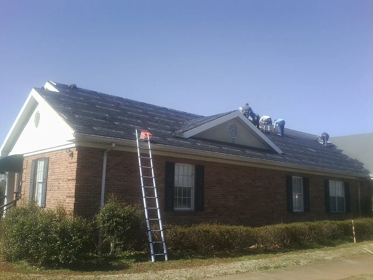 Crew tearing shingles off a brick ranch roof with a ladder set — Metal Roof Repair work by our crew in Morse Bluff