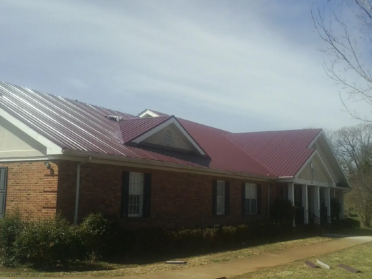 Red metal roof with gabled entries on a long brick building, from a Hail Damage Roof Repair job in Morse Bluff