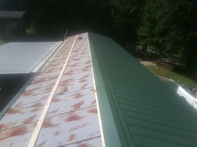 Old rusted panels beside newly installed green metal roofing — Wind Damage Roof Repair by Roofing Brothers in Morse Bluff