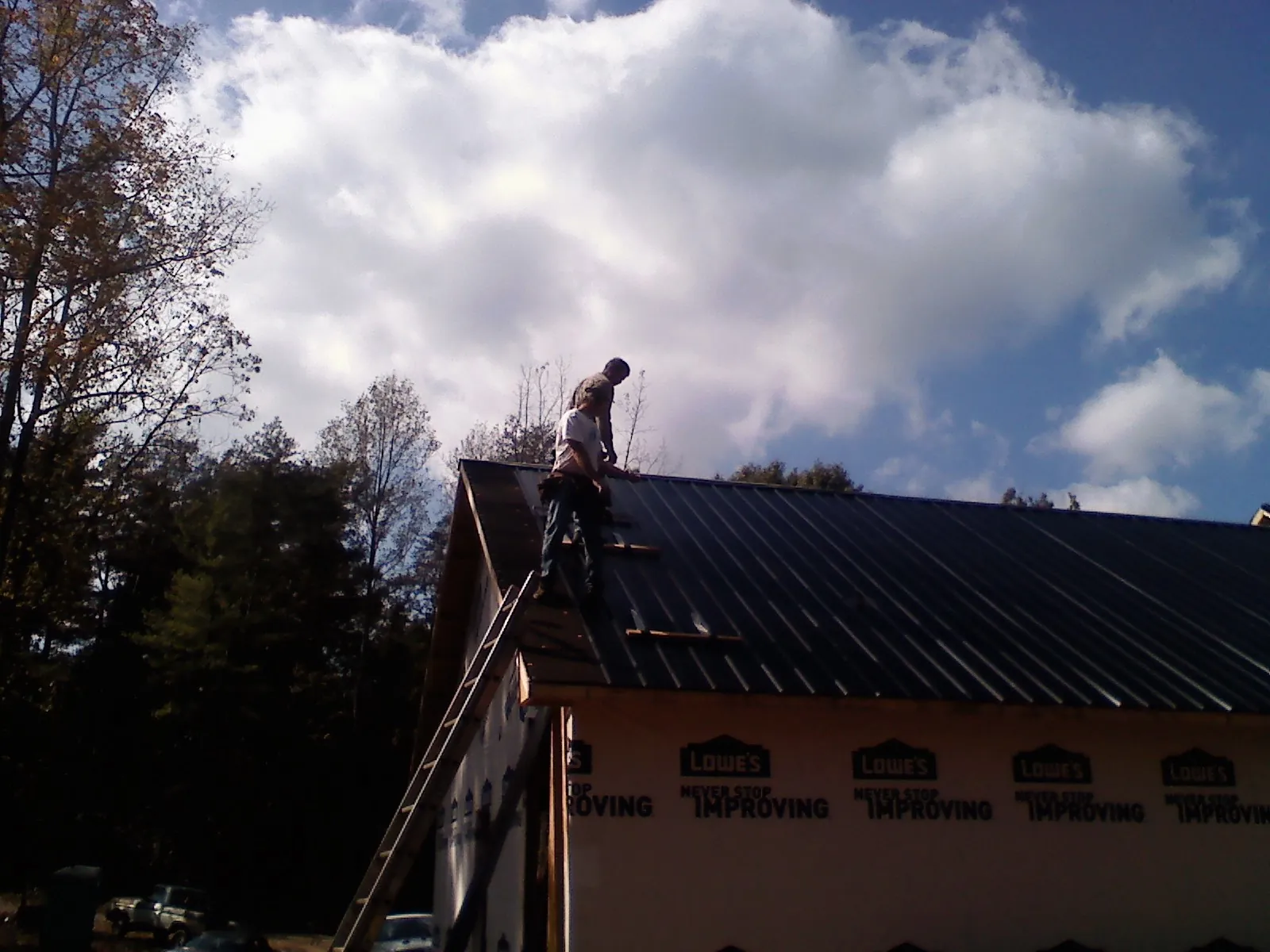 Roofer fastening dark metal panels high against a cloudy sky, from a Roof Inspection job in Morse Bluff