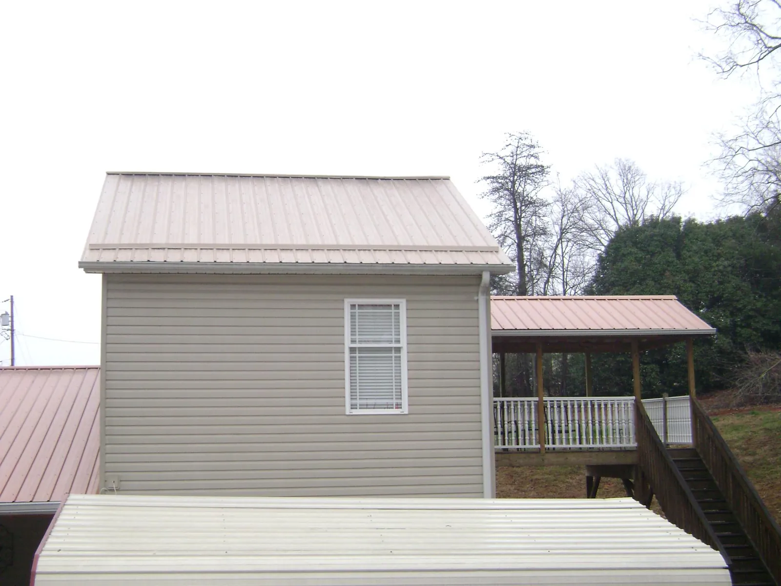 Tan metal roofs on a two story addition and attached porch, from a Roof Replacement job in Morse Bluff
